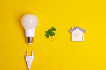 Flat lay composition of LED lamp, leaf, plug and a house symbol on yellow background. Concept for...