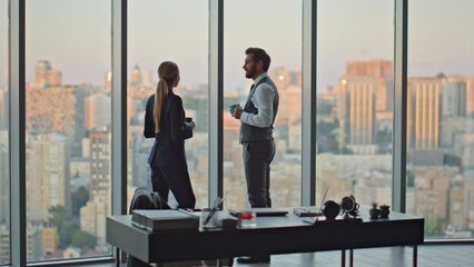 Corporate colleagues enjoying coffee break at evening cityscape. Partners talk