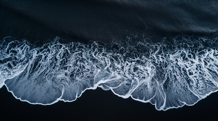 Aerial photography showcasing the rhythmic and tranquil waves gently crashing onto a black sand beach, emphasizing serenity and calmness. 