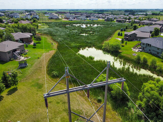 Drone view showing a high voltage power line cutting across a grassed wetland in a residential district.