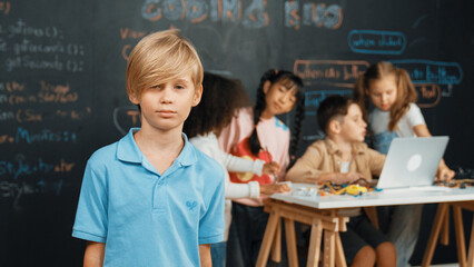 Smart boy looking at camera while diverse friend working or learning engineering code or prompt in...