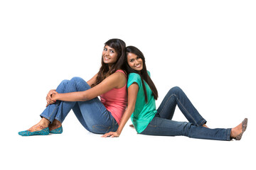 Cheerful young Indian friends sitting with back to each other on floor.