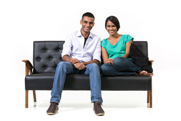 Cheerful young Indian couple sitting on a retro sofa.