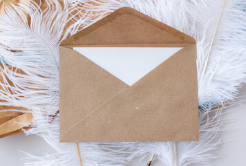 White paper card in craft envelope lying on ostrich feathers, minimalistic mock up flat lay of invitation