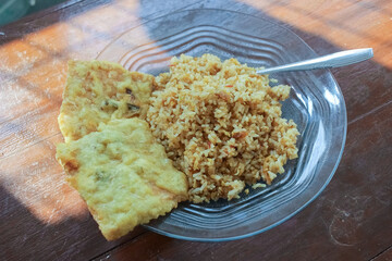 photo of a breakfast dish that is on the table with a menu of egg fried rice with 2 fried tempeh and served in a glass plate