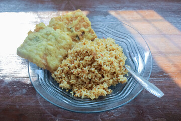 photo of a breakfast dish that is on the table with a menu of egg fried rice with 2 fried tempeh and served in a glass plate