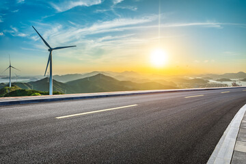 Asphalt highway and wind turbines with mountain natural landscape at sunset. High Angle view. - obrazy, fototapety, plakaty