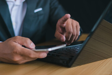 Close-up of a businessman working with a notebook computer and pointing his hand in an office desk...