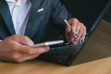 Close-up picture of a businessman working with a laptop and taking notes on his desk in the office.