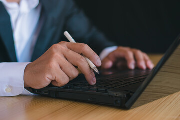 Close-up of businessman working with notebook computer and using pen to take notes in office desk