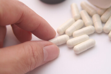 close up of hand holding white capsules on white background with copy space