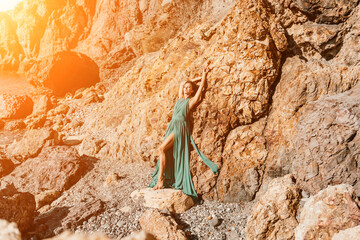 Woman green dress sea. Woman in a long mint dress posing on a beach with rocks on sunny day. Girl on the nature on blue sky background.