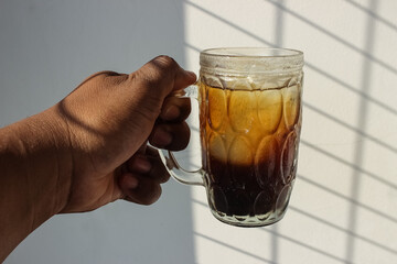 photo of an iced coffee drink in a large glass cup being held by a man against a white wall...