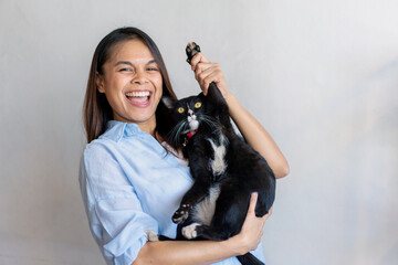 Joyful fit woman sitting having fun with cute cat on the armchair at living room one autumn day , friendship and love for pets.