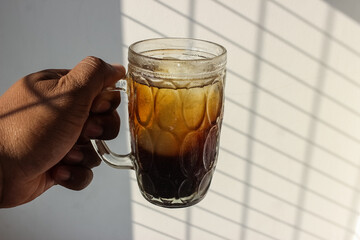 photo of an iced coffee drink in a large glass cup being held by a man against a white wall...