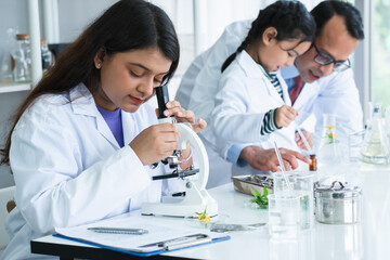 Indian scientist woman student using microscope do an experiment at biology class in school laboratory while teacher teaching another kid student. Education, science and school concept - obrazy, fototapety, plakaty
