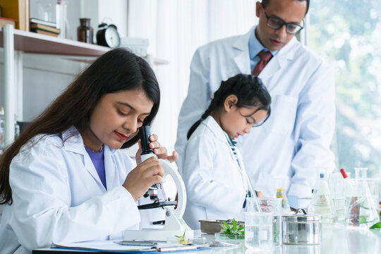 Indian scientist woman student using microscope do an experiment at biology class in school laboratory while teacher teaching another kid student. Education, science and school concept