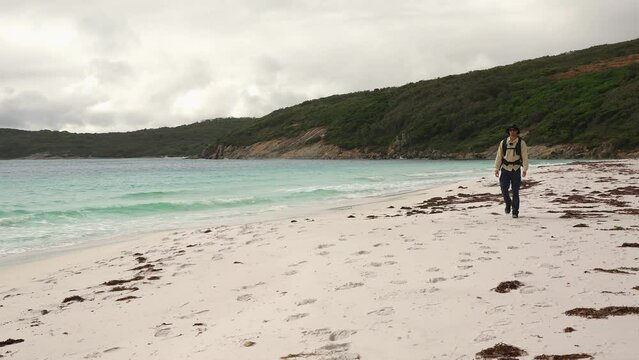 A Man Walking Towards The Camera Along A White Sand Beach In Australia On An Overcast Day.