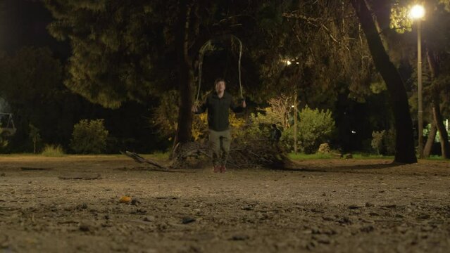 Young man jumping rope skipping in park at night