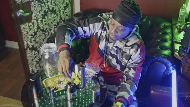 a black man stirs the pot in the bowl of an electronic water bong to allow it to burn better there is a rolling tray on the table