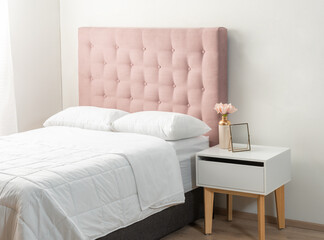 Sophisticated Feminine Bedroom: Plush Pink Tufted Headboard Sets a Delicate Tone, Matched by a Modern White Nightstand with Wooden Legs, Accented by a Pastel Bloom in a Gold Vase.