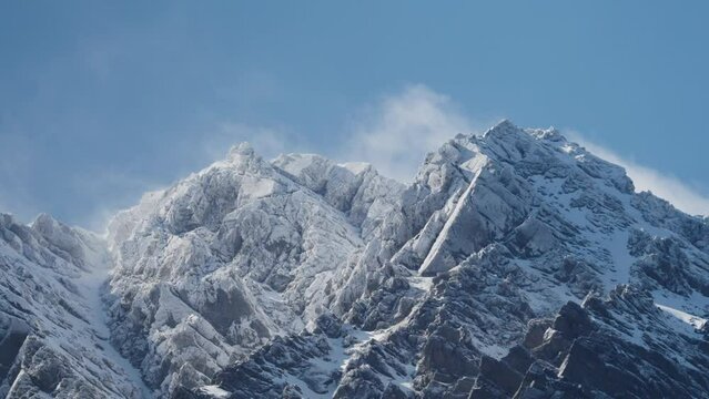 Rugged Snowy Mountains with beautiful clouds rolling over with a big blue sky. It's steep and rocky on a windy day. The Remarkables, New Zealand.