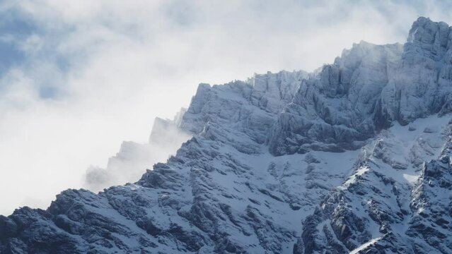 Rugged Snowy Mountains with beautiful clouds rolling over with a blue sky. It's very steep and rocky on a windy day. The Remarkables, New Zealand.