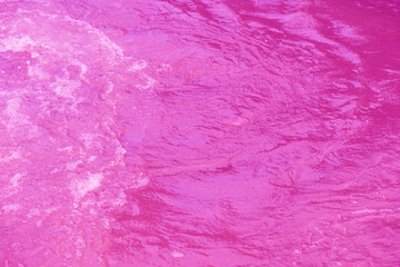 Purple water background. Pink water splashe on the surface ripple blur. Defocus blurred transparent pink colored clear calm water surface texture with splash and bubble. Water waves with shining.