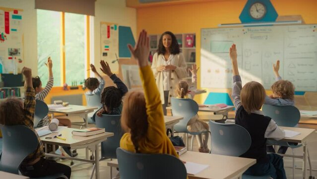 Excited Elementary School Teacher Asking a Diverse Class of Children a Mathematical Question. Smart Kids Raising Hands while Sitting Behind a Desks and Eager to Provide a Solution