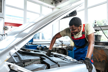 Young African man working under the hood of car fixing engine in auto service