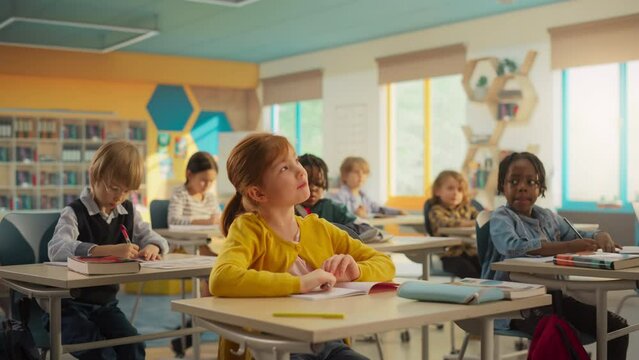 Little Girl Raising Her Hand and Answering Teacher's Question. Primary School with a Group of Smart Multiethnic Kids Sitting Behind Desks, Learning New Things and Acquiring Knowledge