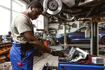 African male auto-mechanic repairing car brakes under the car in auto service