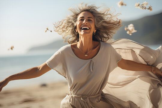  Joyful Elderly Lifestyle Concept. Happy Mature Woman With Arms Outstretched Feeling The Breeze At Beach. Beautiful Middle Aged Woman With Arms Up Dancing On Beach. Mid Lady Feeling Good And Enjoying 