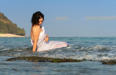 Beautiful woman in white dress sits in the water on ocean shores