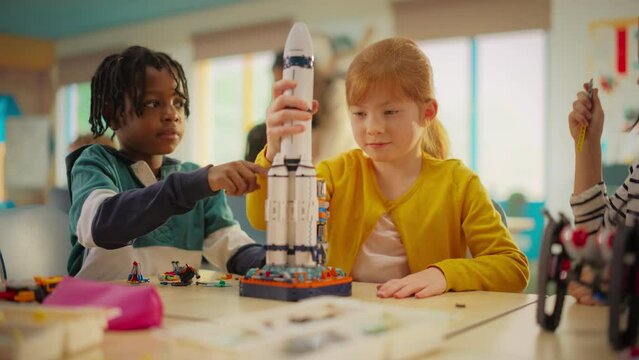 Diverse Primary School Kids Building a Space Rocket Model in Class. Girl Installing the Top Part of the Spaceship and Finishing the Project. Kids High Five After Successfully Accomplishing the Goal