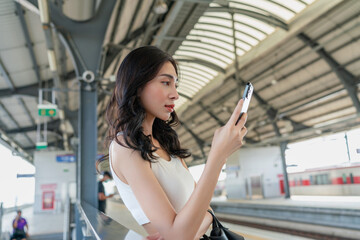 Asian woman using phone for social media while commuting at a train commuter station