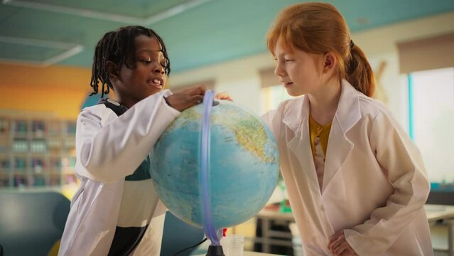 Portrait of a Cute Primary School Caucasian Girl and an African Boy Exploring the World on a Globe. Kids are Conducting Geography Class Research and Learning Important Geopolitical Landmarks
