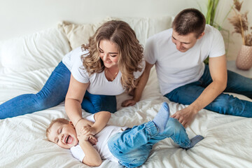 Happy parents tickling son in bright bedroom and laughing - obrazy, fototapety, plakaty