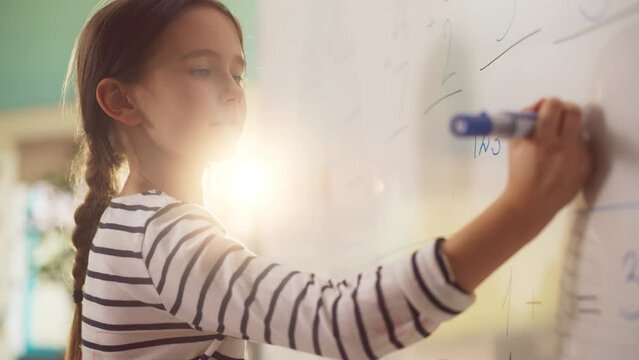 Talented Small Girl Solving an Arithmetic Equation that a Teacher Gave Her. Portrait of a Happy Elementary School Pupil Studying Hard, Writing a Correct Answer on a Whiteboard During a Math Test