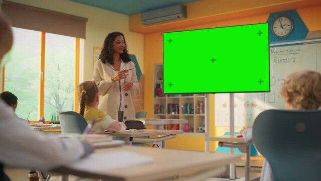 Diverse Primary School Children Learning Mathematics and Geometry in Class. Lesson is Presented by a Young Multiethnic Female Teacher that Shows a Presentation on a TV Display with Green Screen