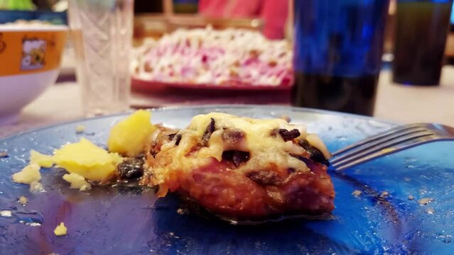 A piece of fried meat with cheese and mayonnaise lies in a plate on the table against the background of a festive table with food, close-up