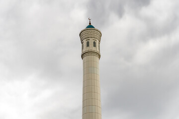 Beautiful high minaret made of white stone against a sky with clouds. Islam and Muslim traditions...