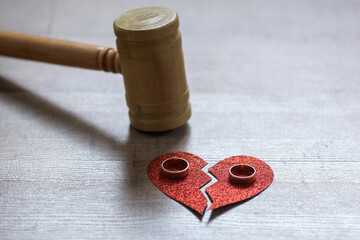 Wedding rings and broken heart paper with a gavel on wooden background. Divorce concept.