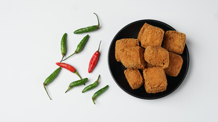 Fried tofu on a black plate with chilies in a white background