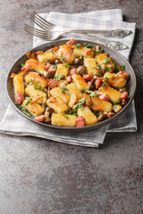 Polish fried potato dumplings Kopytka with bacon, onions and mushrooms close-up in a plate on the table. Vertical