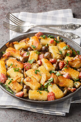 Potato dumplings or kopytka is made with cooked mashed potatoes served with bacon, onions and mushrooms close-up in a plate on the table. Vertical
