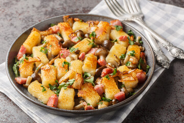 Potato dumpling originating from Poland kopytka served with bacon, onions and mushrooms close-up in a plate on the table. Horizontal