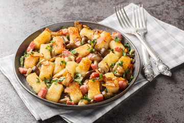 Kopytka Polish dumplings or little hooves made of mashed potatoes served with bacon, onions and mushrooms close-up in a plate on the table. Horizontal