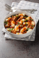 Polish traditional potato dumplings Kopytka with goulash close-up in a plate on the table. Vertical