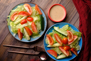 fresh raw vegetable salad. iceberg lettuce, sliced tomatoes, sliced cucumber and cherry tomatoes with peanut sauce salad dressing.